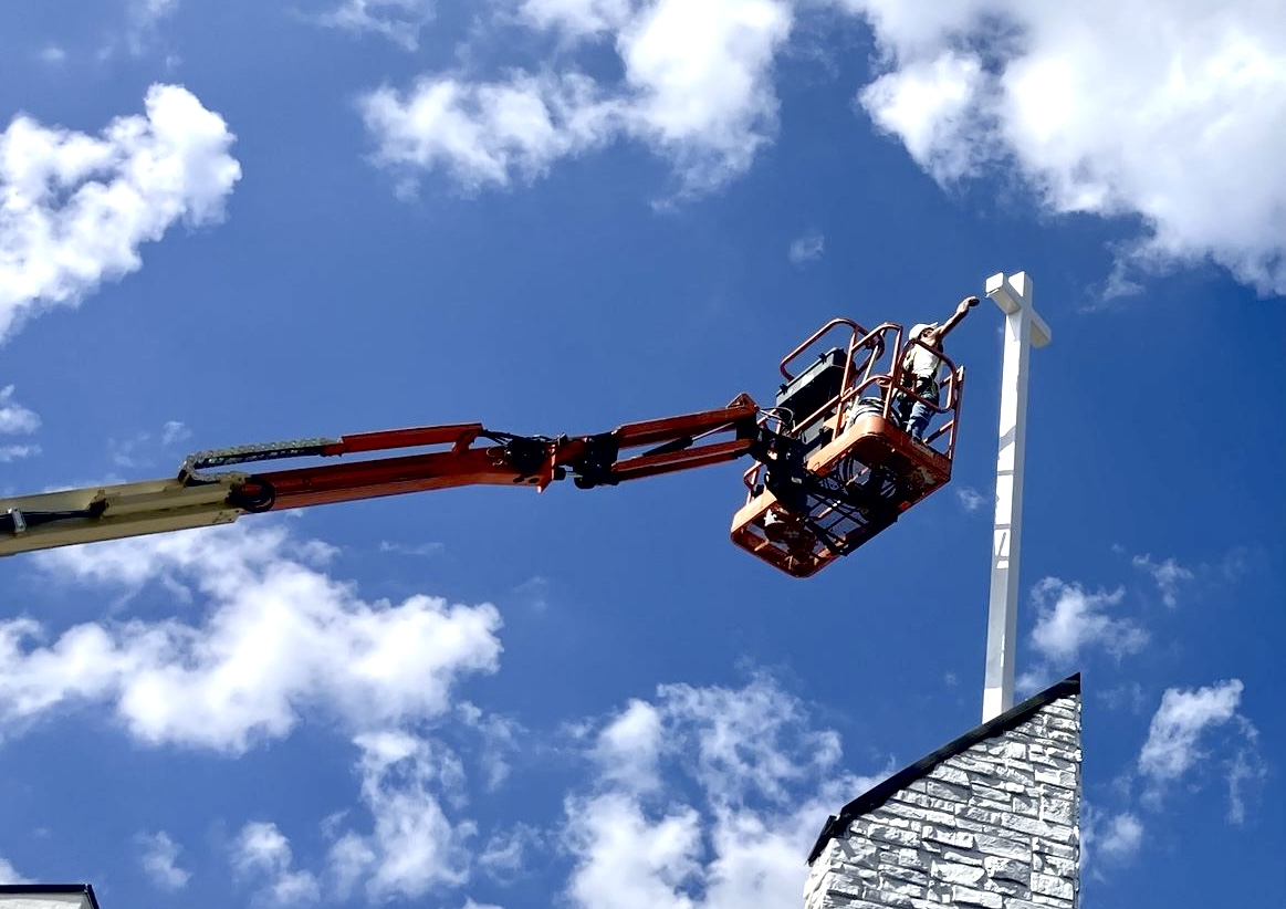 Spray GenX lift painting a church cross against a blue sky